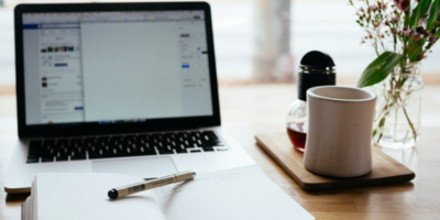 Computer with open notebook in front of it and a cup of coffee to the side